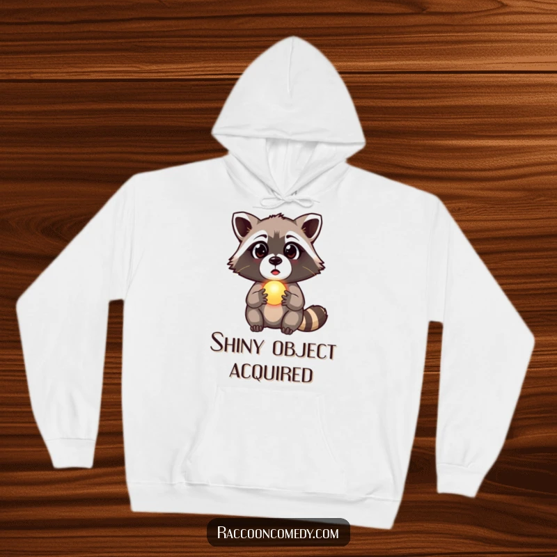 Funny raccoon hoodie featuring a surprised raccoon clutching a tiny, glowing orb, embodying mystery and wonder, a warm funny gift.