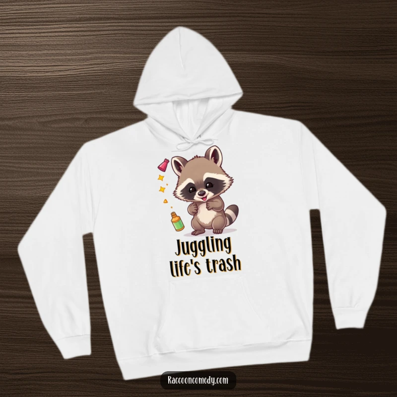 Funny hoodie featuring a joyful raccoon juggling assorted shiny objects, perfect for those who love a bit of sparkle.