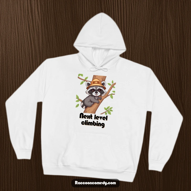 Funny hoodie with a cheerful raccoon cub in an explorer hat, climbing a tree, offering warmth and a dose of adventurous cartoon humor.