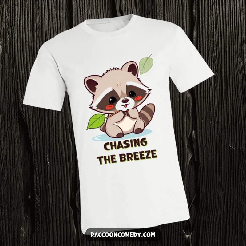 Funny kawaii raccoon playfully batting at a floating leaf with a happy expression, printed on a comfortable t-shirt.