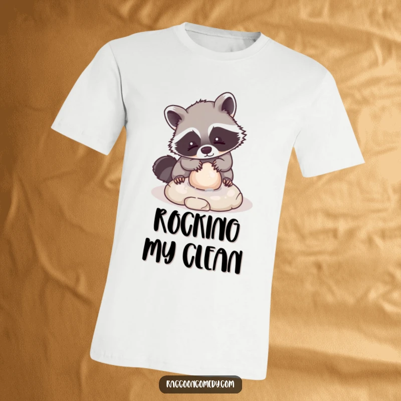 Funny T-shirt featuring a very cute, kawaii raccoon character meticulously washing a small, round stone, designed to spread joy and charm.